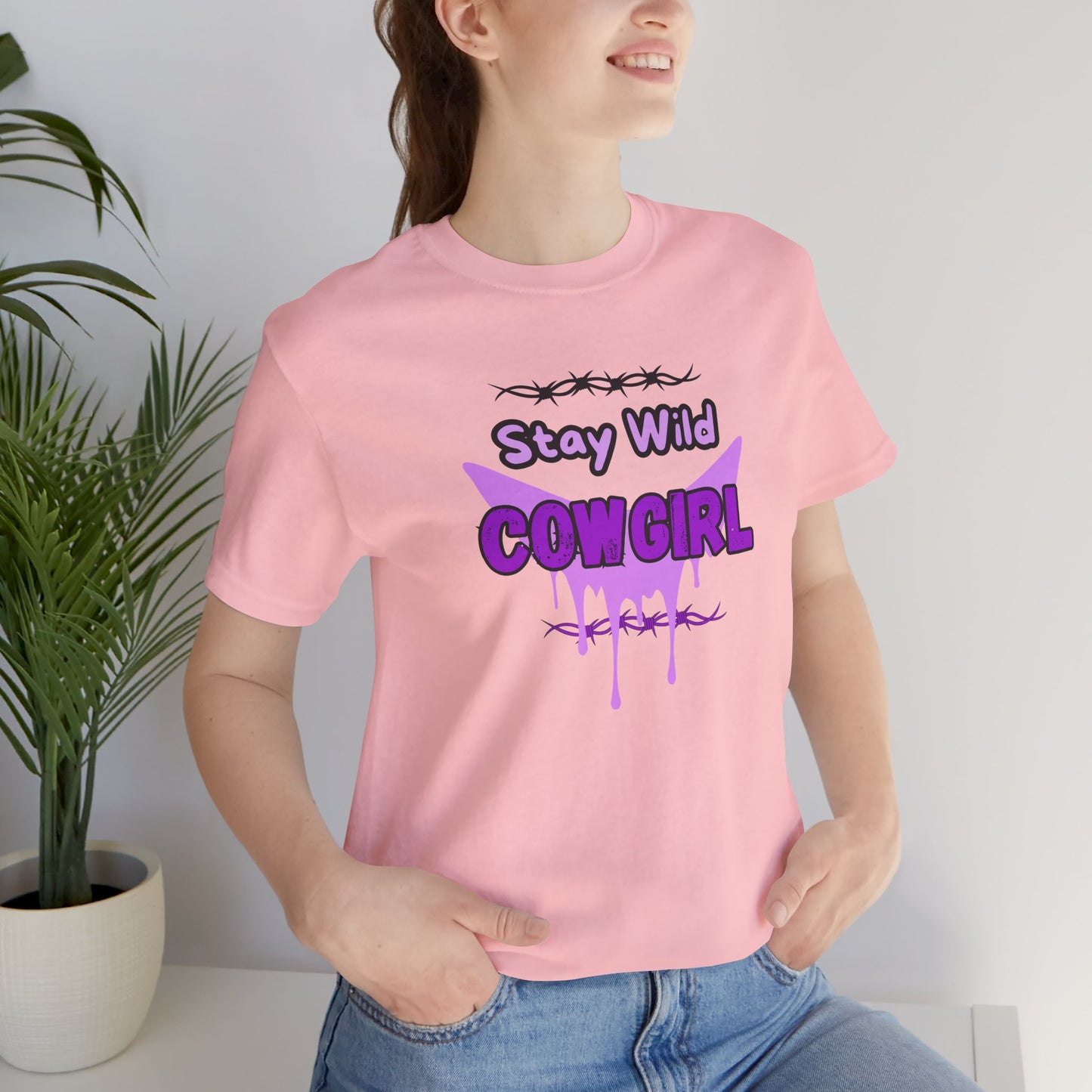 A model wearing a pink Cowgirl Western Tee featuring a bold 'Stay Wild COWGIRL' graphic with barbed wire design.